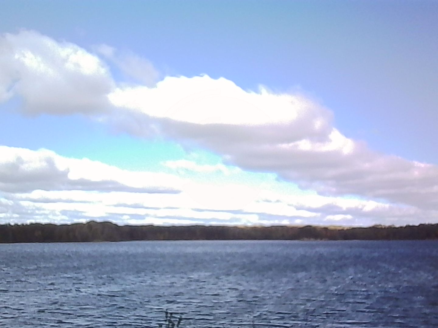 Full white clouds in a blue sky over the water kicked up by a strong wind.
