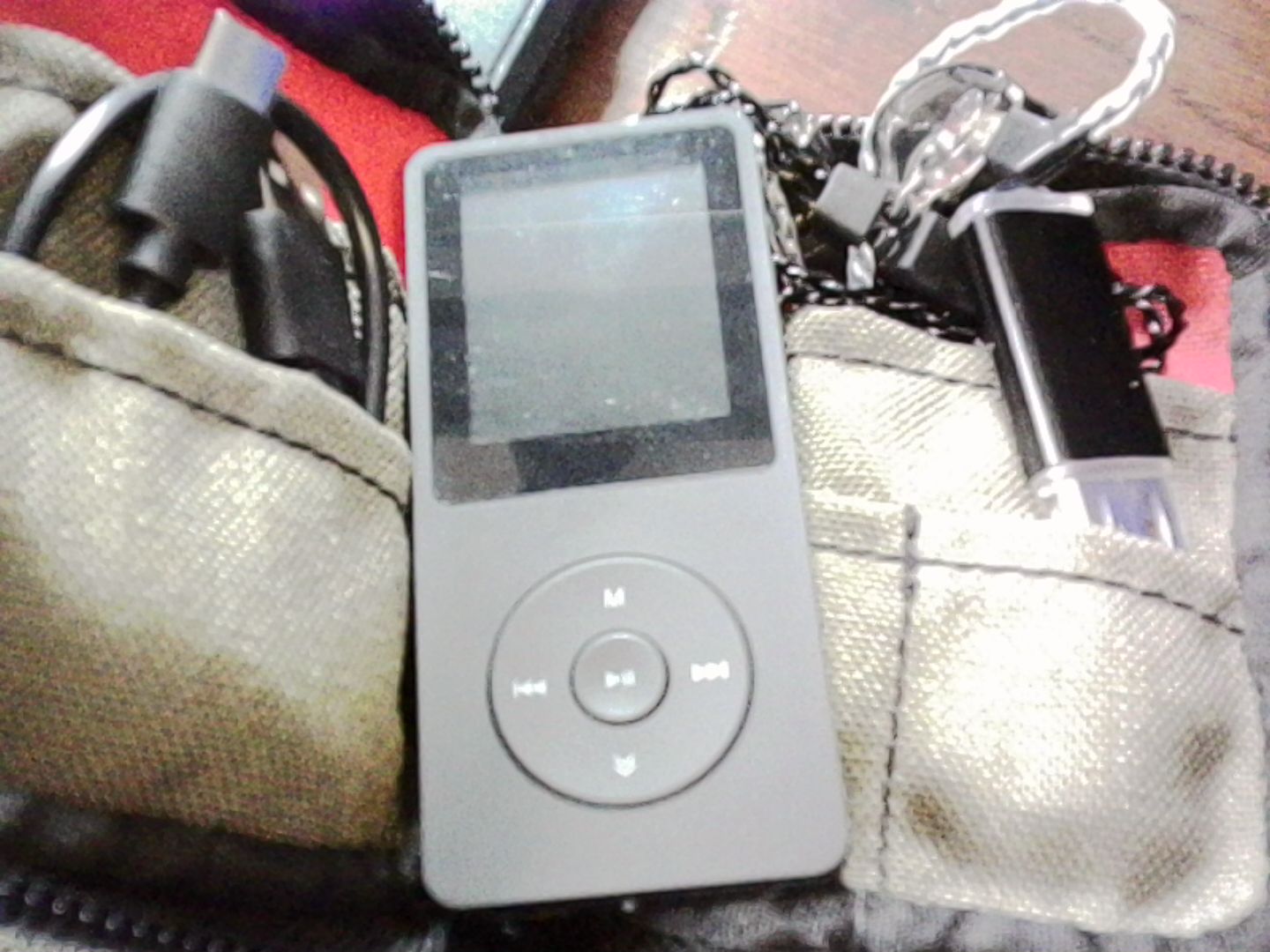 Black MP3 player with a small screen and scroll wheel style interface sitting on top of a small case containing a cable and headphones. Black MP3 player with a small screen and scroll wheel style interface sitting on top of a small case containing a cable and headphones