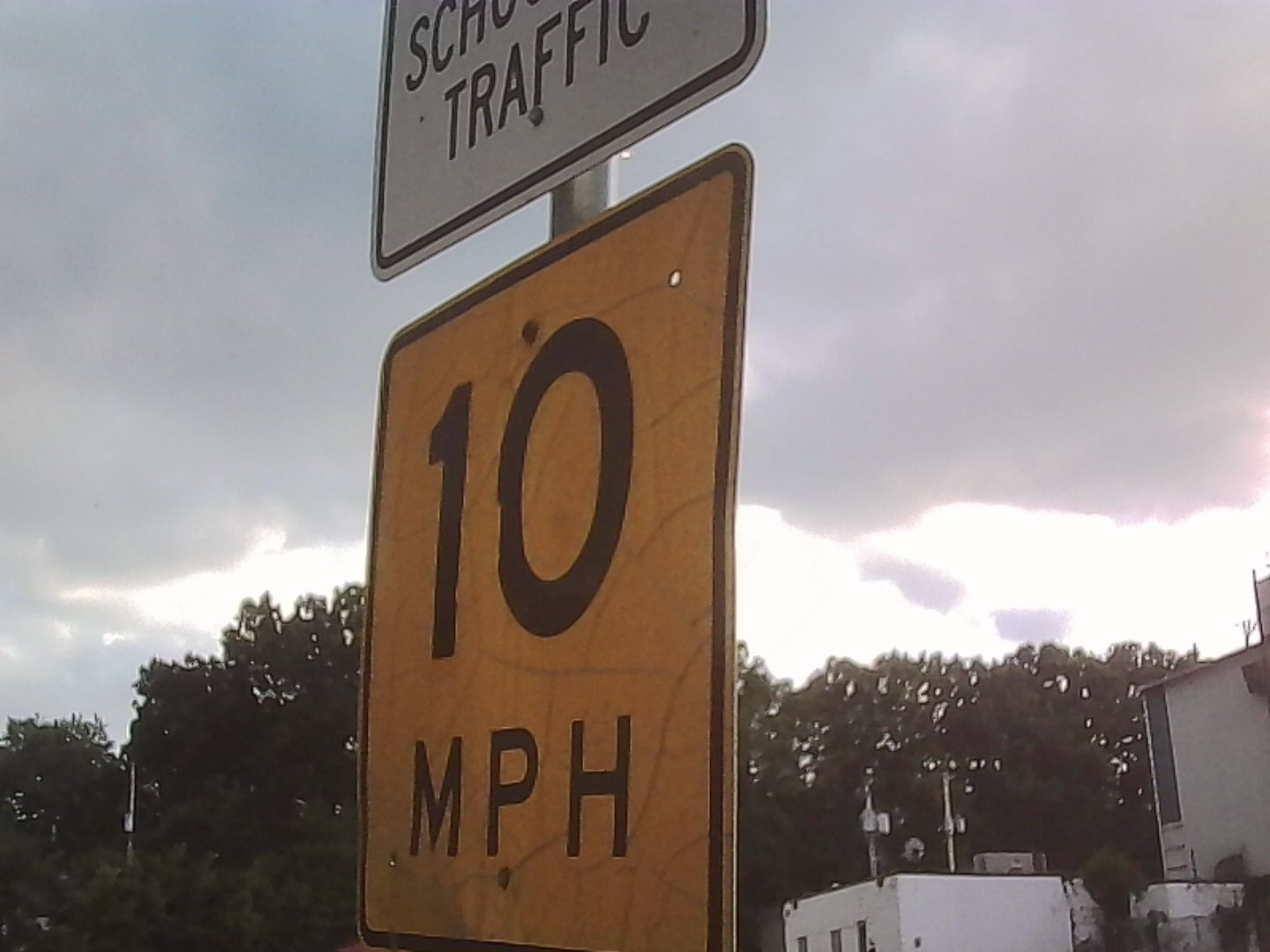A yellow 10 MPH suggested speed limit sign. Out of frame is the bus lot for the local school.